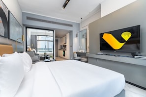 Ein modernes Hotelzimmer mit einem großen Bett, einem an der Wand befestigten Fernseher und Blick auf die Stadt durch das Fenster.