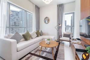 Una sala de estar moderna con sofá, una mesa de centro, televisor y vistas a la ciudad a través de amplias ventanas.