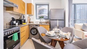 A compact kitchen with a stove, oven, washing machine, and a refrigerator. There is a dining area with a table set for two.