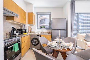 A compact kitchen with a stove, oven, washing machine, and a refrigerator. There is a dining area with a table set for two.