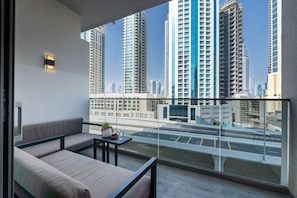 A balcony with a sofa and a small table, overlooking a cityscape with tall buildings.