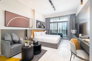 A modern hotel room with a large bed, a sofa, a desk, and a TV.