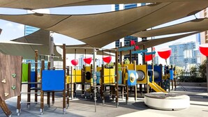 Un espace de jeux extérieur doté de diverses installations, notamment des toboggans et des structures d’escalade, le tout abrité sous une pergola ombragée.
