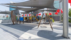 Un espace de jeux extérieur doté de diverses installations, notamment des toboggans et des zones d’escalade, le tout abrité par de grandes structures ombragées.