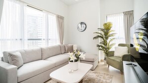 A modern living room with a sofa, a coffee table with flowers, a TV, and a potted plant.