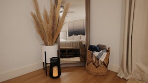 Una habitación con cama, espejo, un florero con plumas de pluma, una vela y una cesta de mimbre con ropa.