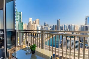 A balcony with a view of a city skyline, a table with a glass top, and a potted plant.