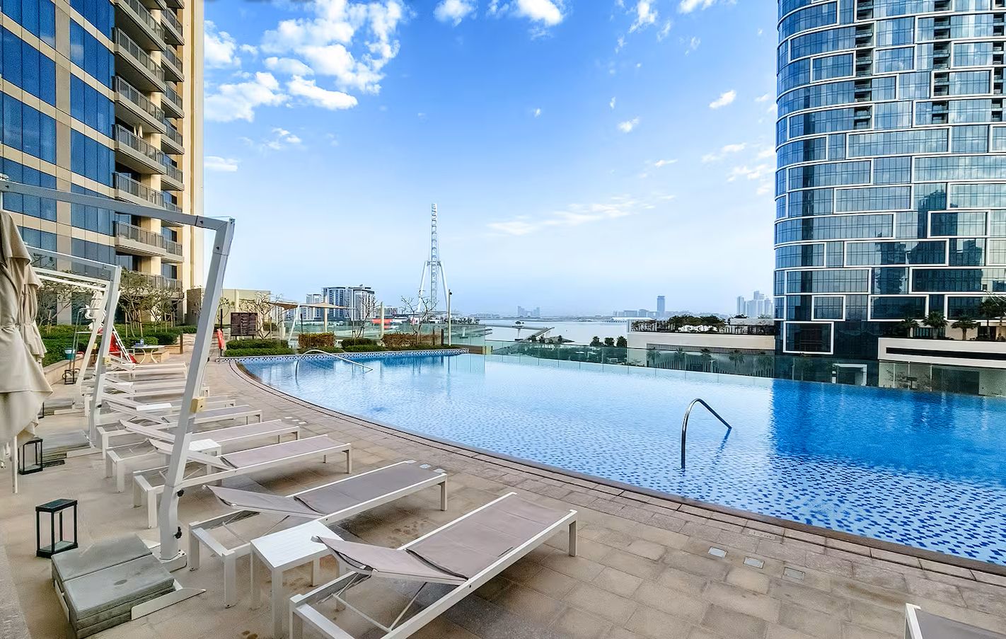 Une piscine à débordement située sur le toit, avec des chaises longues, une vue sur les gratte-ciel de la ville et un ciel dégagé.