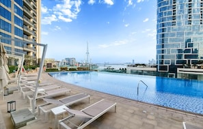 A rooftop infinity pool with lounge chairs, a view of the city skyline, and a clear sky.