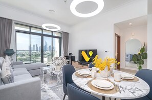 A modern living room with a city view, a dining area with a table set for four, and a flat-screen TV.