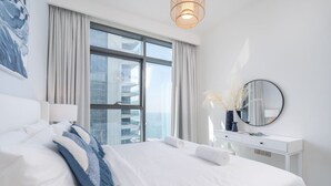 Ein modernes Hotelzimmer mit einem großen Bett, einer weißen Kommode, einem runden Spiegel und Blick auf die Stadt durch große Fenster.