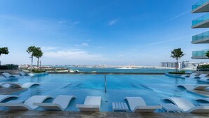 Ein Pool mit Liegestühlen und Blick auf das Meer und die Skyline der Stadt.