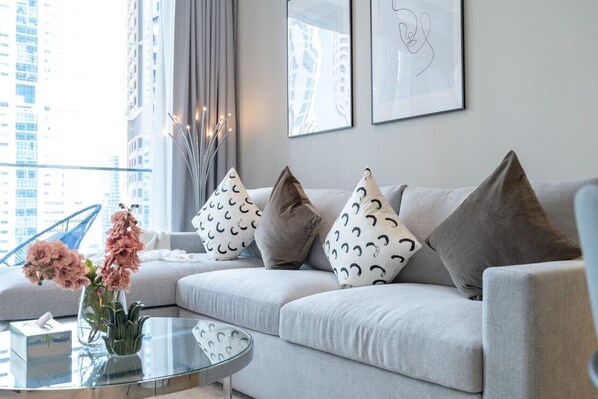 Un salon moderne avec un canapé gris, des coussins à motifs, une table basse en verre et un vase rempli de fleurs.