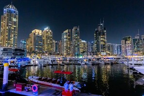 Un puerto deportivo con barcos amarrados, un horizonte urbano con edificios iluminados y un cielo nocturno despejado.