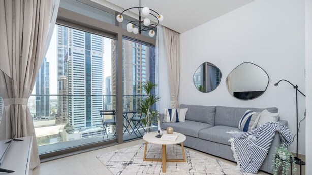 Una sala de estar moderna con un sofá gris, una mesa de centro redonda y un ventanal con vistas a la ciudad.