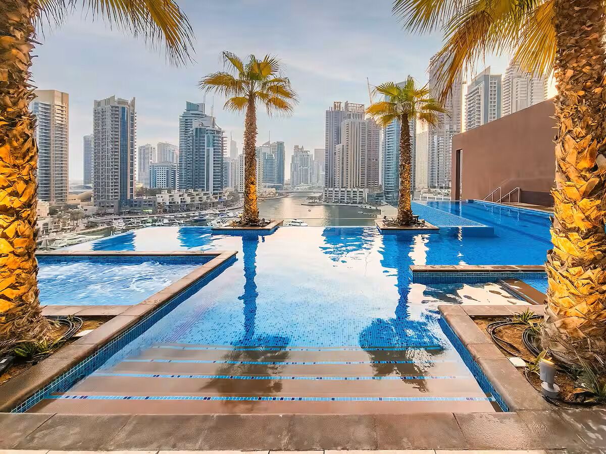 Ein Rooftop-Pool ohne Rand mit Palmen, mit Blick auf eine Skyline mit Hochhäusern.