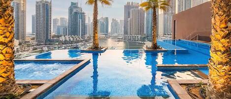 A rooftop infinity pool with palm trees, overlooking a cityscape with high-rise buildings.