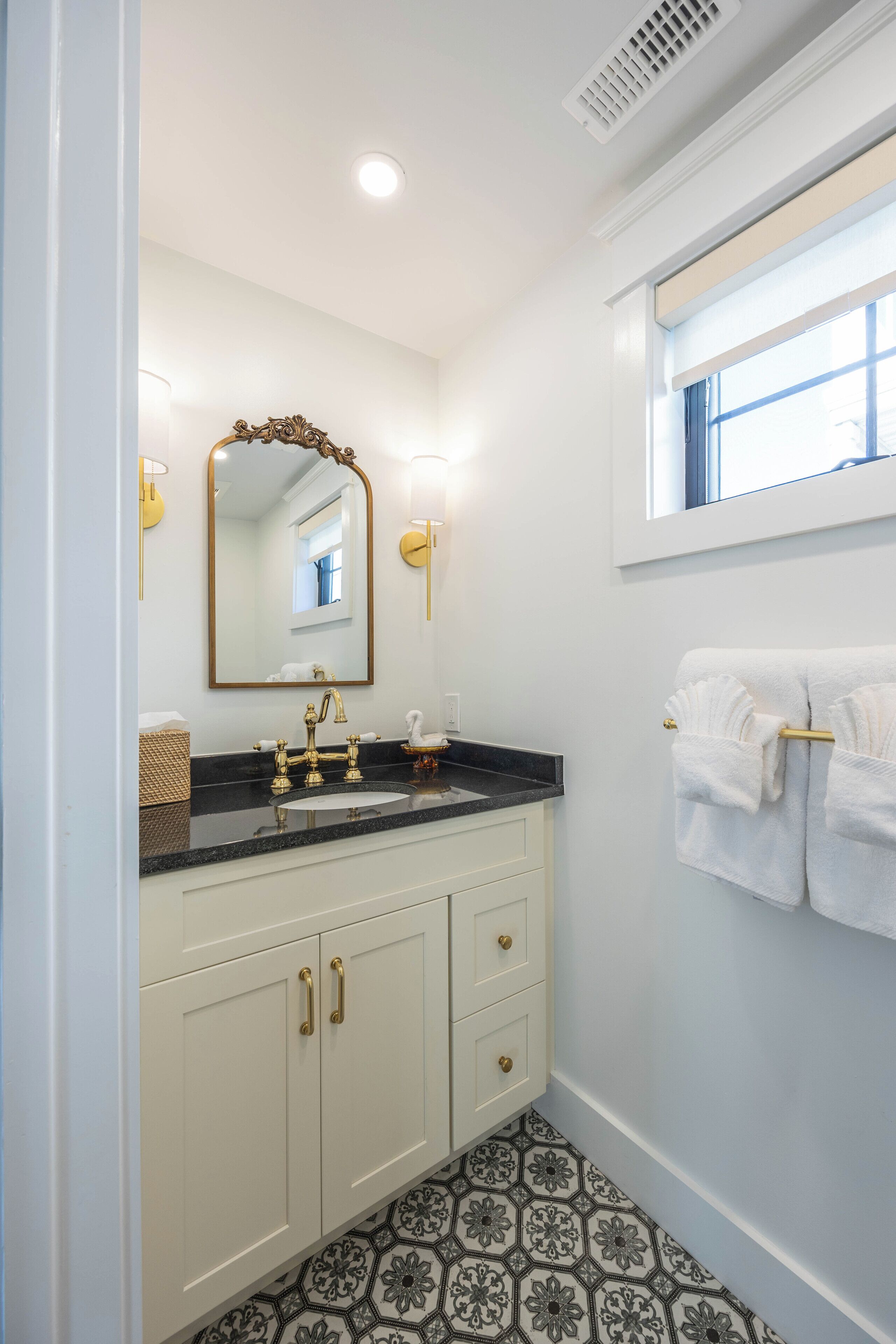 A bathroom with a white vanity, gold fixtures, and a patterned floor.
