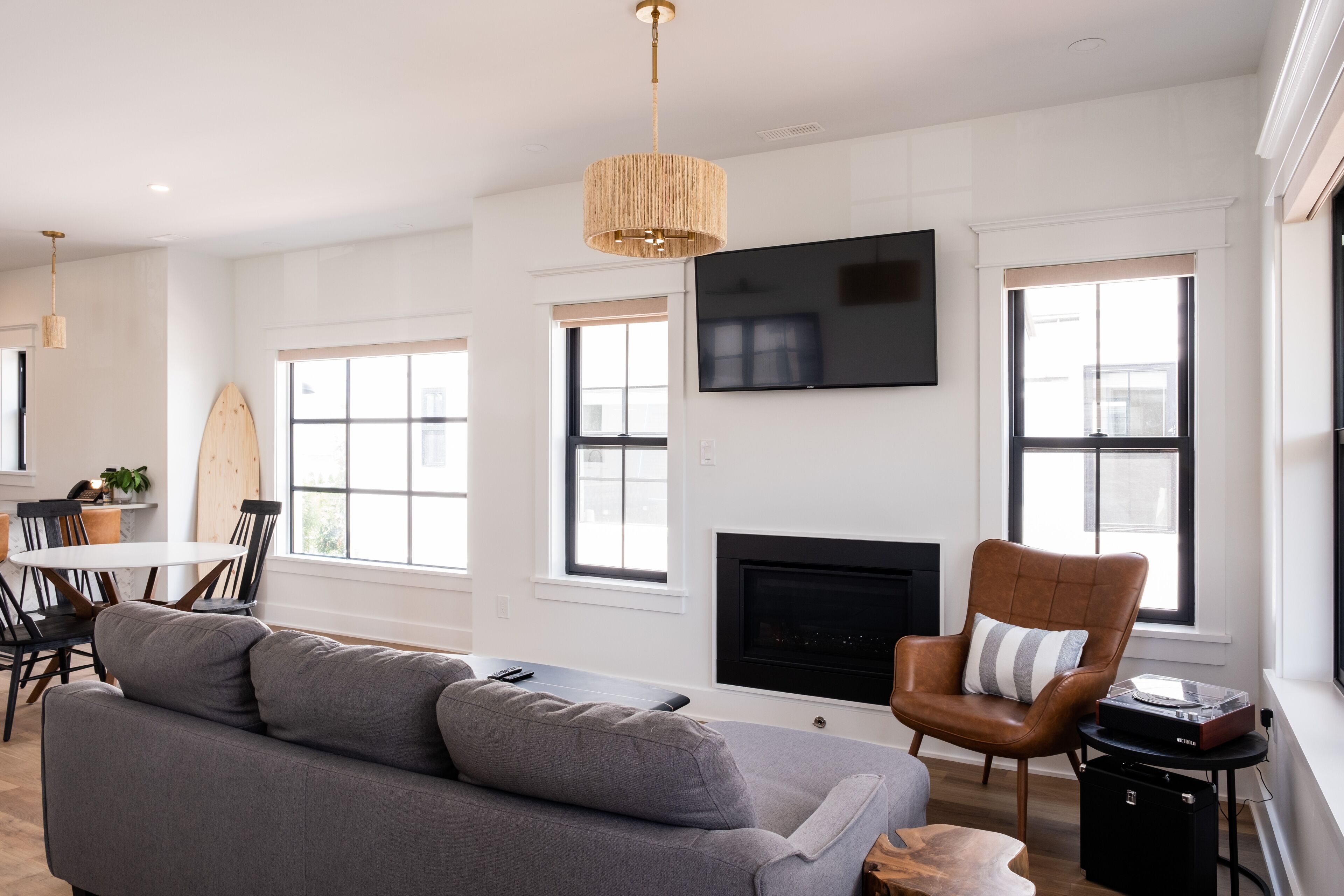 A modern living room with a grey sofa, a brown leather chair, a round dining table, and a fireplace.