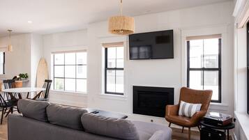 A modern living room with a grey sofa, a brown leather chair, a round dining table, and a fireplace.