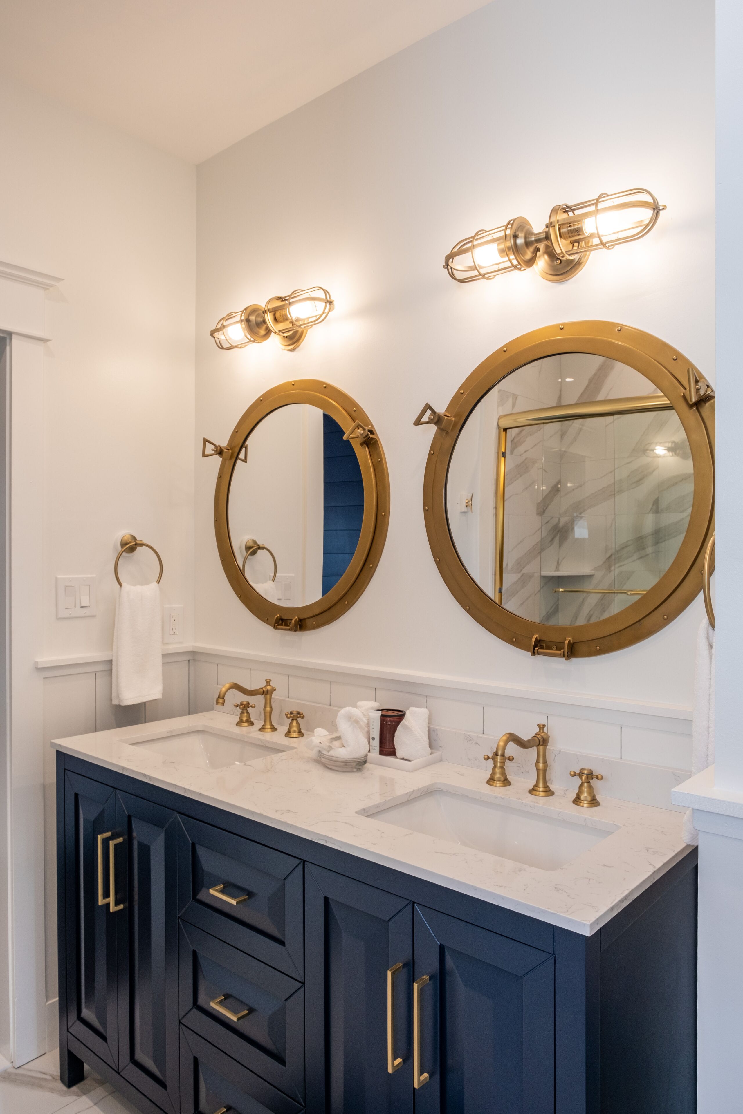 A bathroom with two round mirrors, a white sink with gold fixtures, and dark blue cabinets.