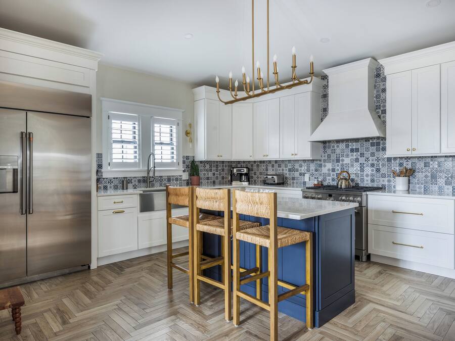 Eine moderne Küche mit weißen Schränken, einem Edelstahlkühlschrank, einer blauen Kochinsel mit Barhocker und einer gemusterten Spritzschutzwand.