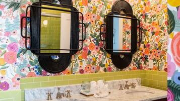 A bathroom with a floral wallpaper, two mirrors with black frames, a marble sink, and wooden cabinets with gold handles.