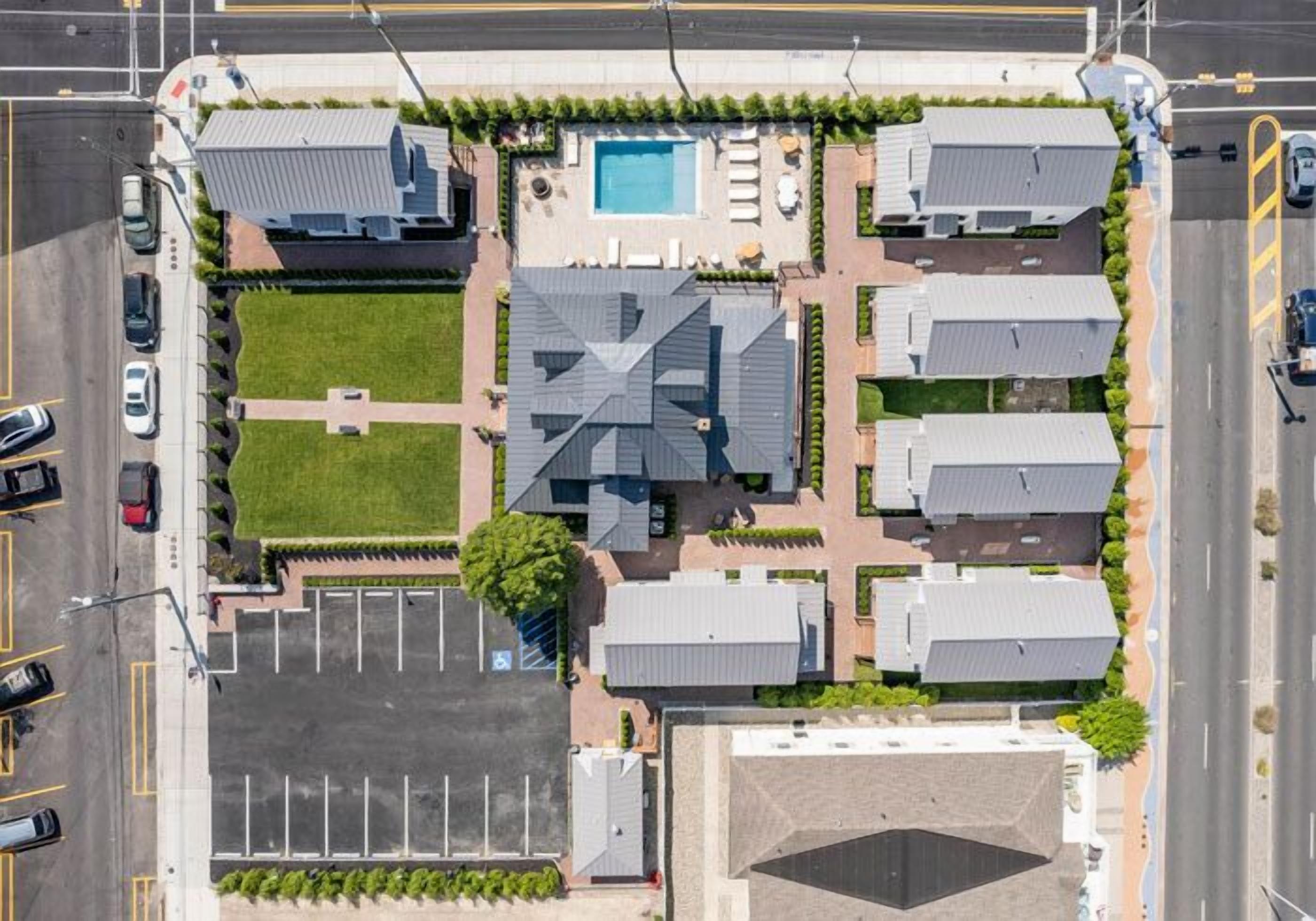 An aerial view of a hotel with a swimming pool, multiple parking lots, and a central courtyard.
