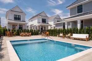 A swimming pool with a wooden deck, lounge chairs, and a fence. - The Hen Houses (Wildwood)