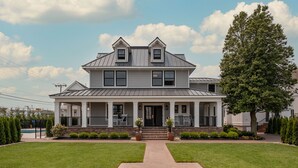 A two-story house with a front porch, a large lawn, and a tree. - The Hen Houses (Wildwood)