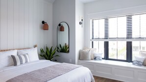 A bedroom with a large bed, a window with blinds, a mirror, and a plant. - The Hen Houses (Wildwood)