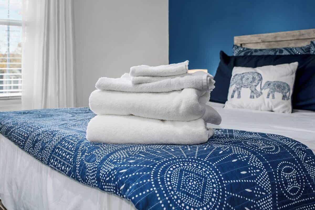 A neatly made bed with a blue patterned bedspread and a stack of white towels on it.