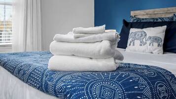 A neatly made bed with a blue patterned bedspread and a stack of white towels on it.