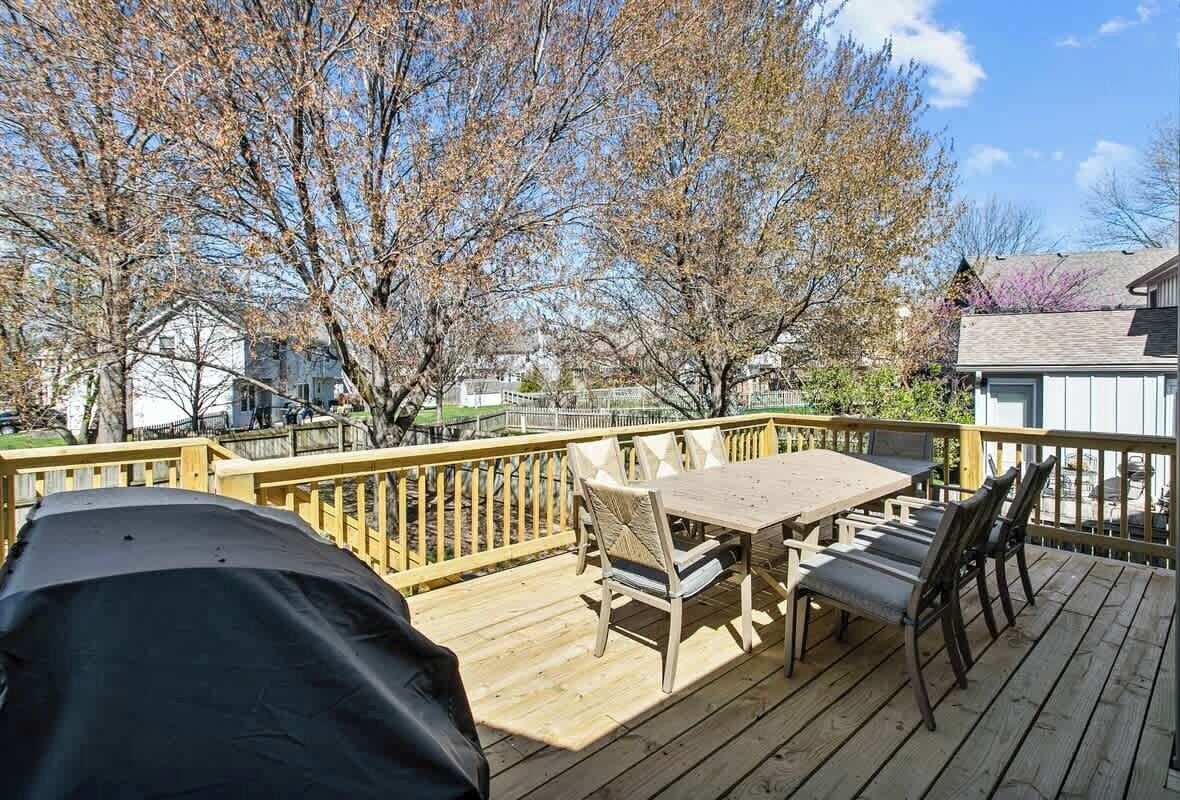 A wooden deck with a table and chairs, surrounded by trees and a fence.