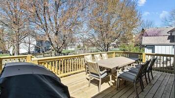 A wooden deck with a table and chairs, surrounded by trees and a fence.