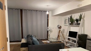 Una sala de estar moderna con un sofá, una mesita, un televisor sobre un mueble bajo, un ventilador y una estantería.