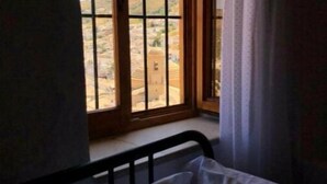 Ein Zimmer mit Bett, einem Fenster mit Blick auf eine Wüstenlandschaft und einem teilweise zurückgezogenen Vorhang.