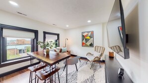 A modern dining area with a wooden table, bar stools, a vase with flowers, and a large window. - King Beds|Parking|0.6 miles from UofL|Free WiFi (Louisville)