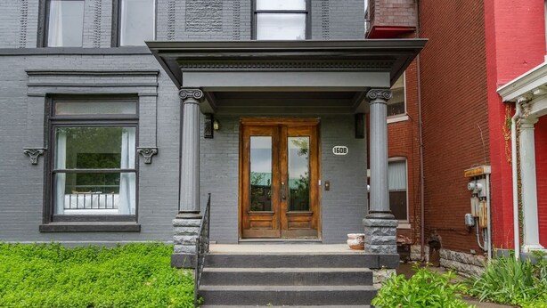 A two-story building with a gray facade, a wooden front door, and a number '1608' on the wall. - King Beds|Parking|0.6 miles from UofL|Free WiFi (Louisville)