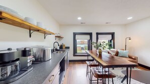 A modern kitchen with a stove, sink, and wooden shelves. There is a dining area with a table and chairs, and a window with a view. - King Beds|Parking|0.6 miles from UofL|Free WiFi (Louisville)