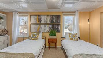 Un dormitorio con dos camas, un cuadro abstracto grande, una mesita con una planta y una ventana con cortinas.