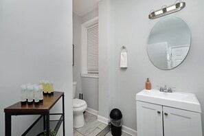 A bathroom with a white sink, mirror, and toilet. There is a small table with bottles and a trash can. - Bridgeport Boho Chic Vibes (Chicago)