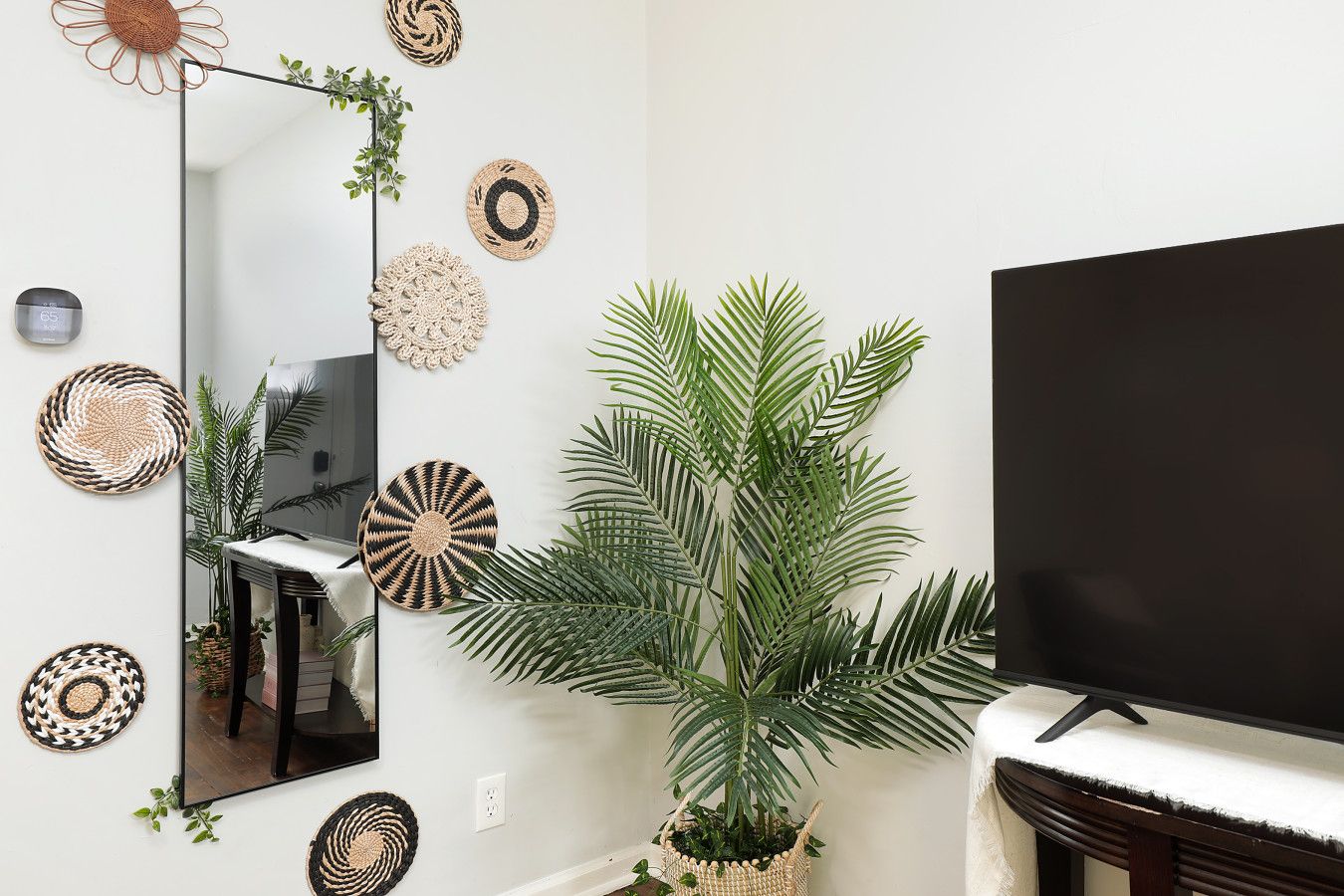 A living room with a large mirror, a flat-screen TV, and several woven wall decorations.