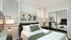 Ein modernes Schlafzimmer mit Bett, Nachttischen, einem Spiegel und Kunstwerken an den Wänden.
