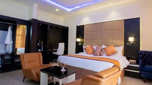 A modern hotel room with a large bed, a desk, two chairs, and a wardrobe. - Princess Luxury Hotels (Ilorin)