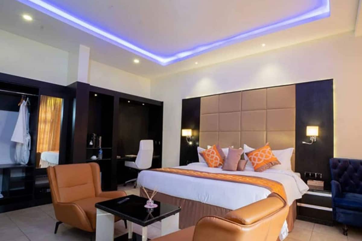 A modern hotel room with a large bed, a desk, two chairs, and a wardrobe.