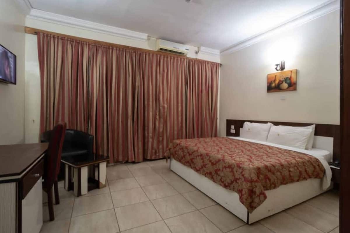 A hotel room with a bed, a desk, a chair, and curtains.