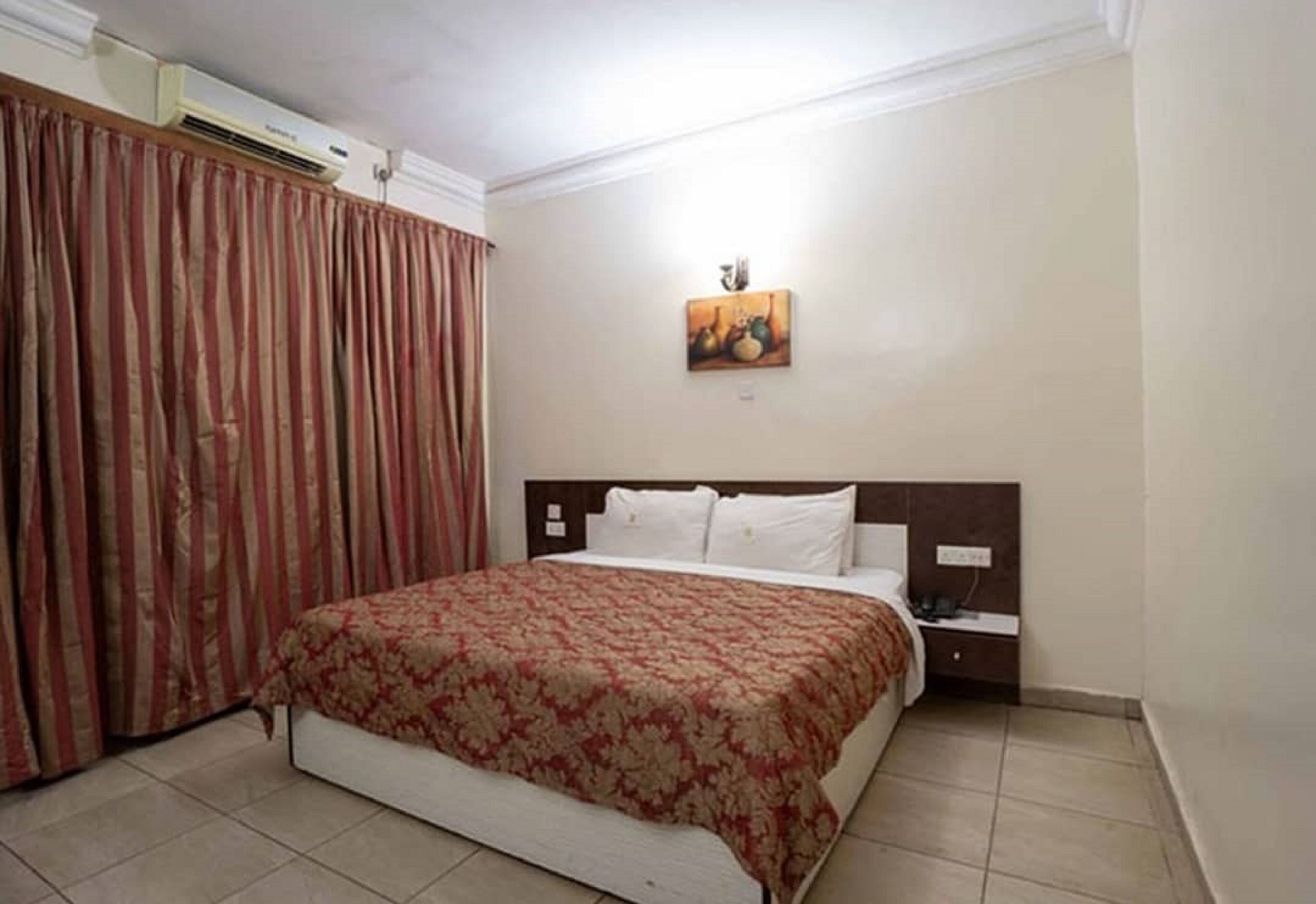 Une chambre d’hôtel avec un lit, une table de chevet, une lampe fixée au mur et un tableau.