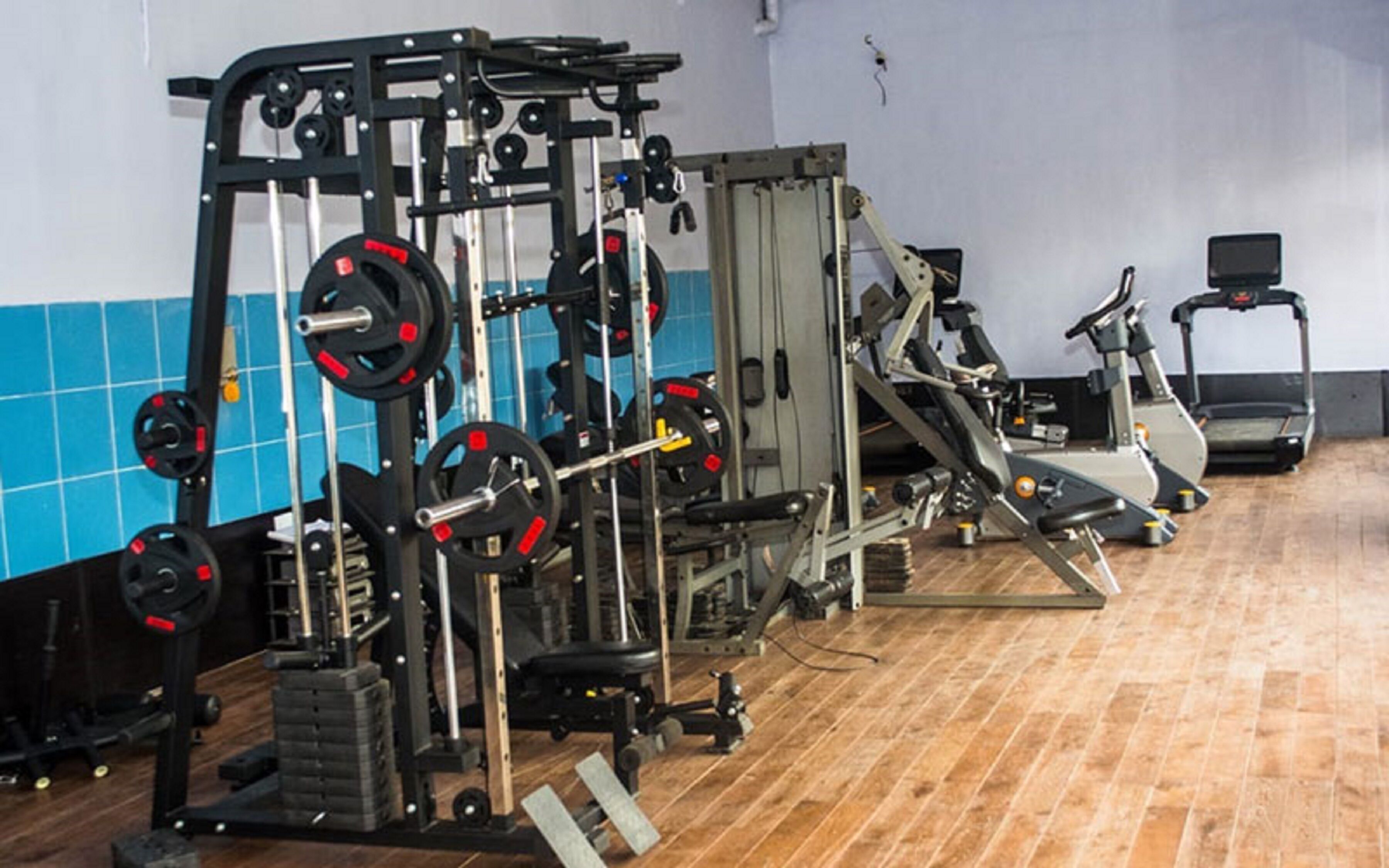 Un gimnasio con equipo de levantamiento de pesas, cintas de correr y una pared con azulejos azules.