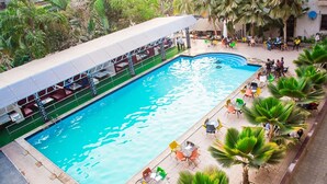 A swimming pool with a covered seating area and palm trees. - Princess Luxury Hotels (Ilorin)